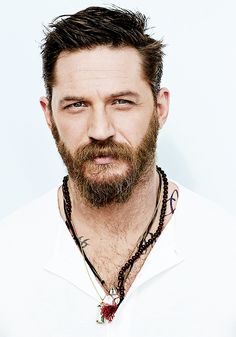 a man with a beard wearing a white shirt and beaded necklace on his neck