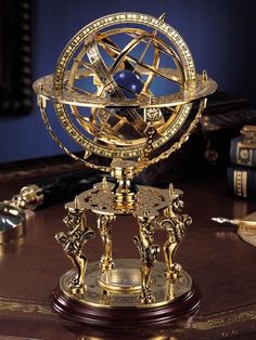 a golden clock sitting on top of a wooden table next to books and a pen