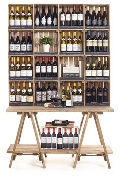 a wooden table topped with lots of bottles of wine next to a shelf filled with bottles