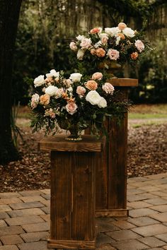 an arrangement of flowers is placed on top of a wooden box in front of a tree