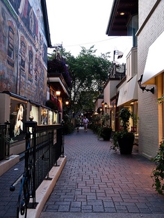 an alley way with shops and people walking on the sidewalk in front of it at dusk