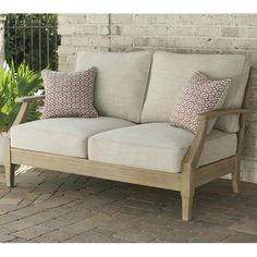 a wooden couch sitting on top of a brick floor next to a potted plant