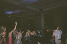 a group of people dancing at a party with their arms in the air and one person holding up a cell phone