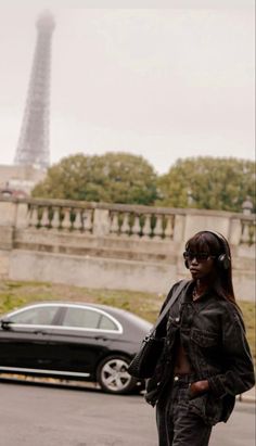 a woman walking down the street with headphones in her ears and a black car behind her