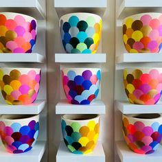 colorful bowls are on shelves in a room with white shelving and painted wallpaper