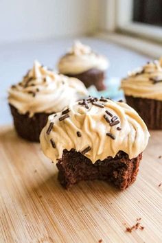 three cupcakes with frosting and sprinkles on a cutting board