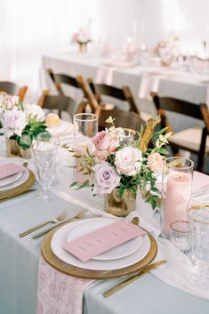 the table is set with pink and white flowers in vases, gold rimmed plates, and napkins