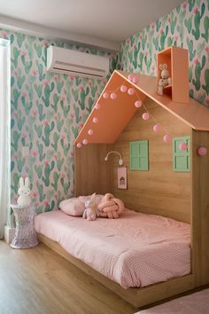 a child's bedroom with cactus wallpaper and pink bedding, including a wooden doll house