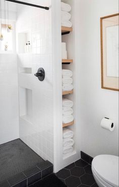 a white toilet sitting next to a walk in shower under a bathroom mirror on top of a wooden shelf