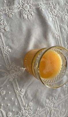 a glass filled with liquid sitting on top of a white table cloth next to a cup