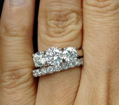 a woman's engagement ring with three diamonds on top of her wedding band,