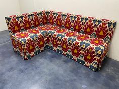 a red, blue and yellow patterned couch sitting on top of a cement floor next to a white wall