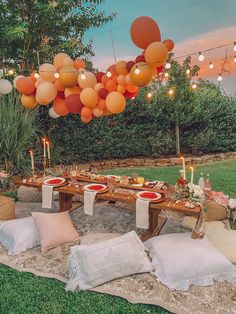 an outdoor table set up for a party with orange and white balloons hanging from the ceiling