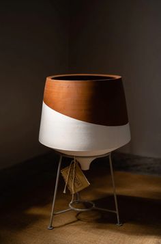 a brown and white pot sitting on top of a metal stand next to a wall