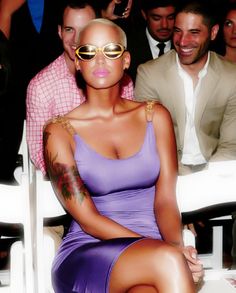 a woman sitting in front of a group of people at a fashion show wearing sunglasses