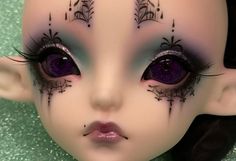 a close up of a doll face with purple eyeliners and black eyelashes on it's head