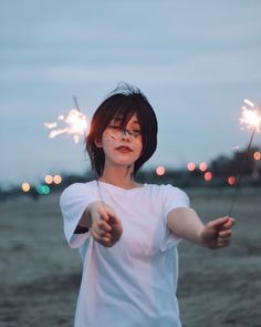 a woman holding two sparklers in her hand and pointing at the camera with both hands