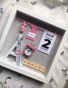 a white frame with pink items in it and a ruler on the wall next to it