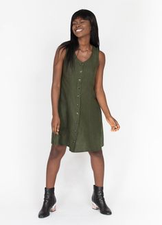 a woman standing in front of a white background wearing a green dress and black boots