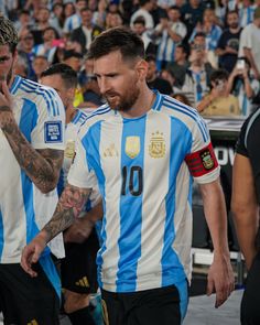 two soccer players are walking together in front of a large group of people with tattoos on their arms