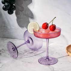 a pink cocktail with cherries and lime in a glass on a marble counter top