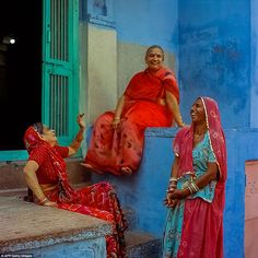 two women sitting on steps in front of a blue building and one is pointing at another woman