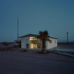 a small building sitting on the side of a road next to a palm tree in front of it