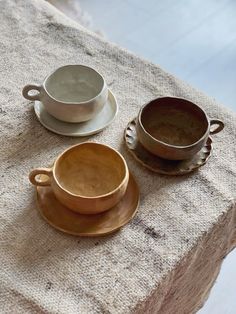 two cups and saucers sitting on top of a cloth covered tablecloth next to each other