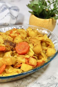 a glass bowl filled with pasta and carrots on top of a table next to a potted plant