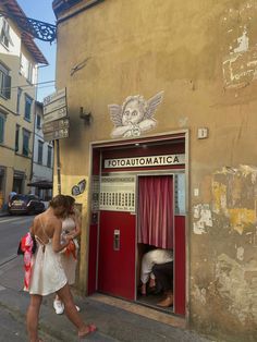 a woman walking past a red door on the side of a building next to a street