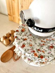 a white mixer sitting on top of a table next to wooden spoons and eggs