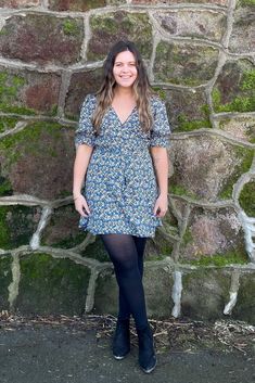 a woman standing in front of a stone wall with her hands on her hips and smiling at the camera