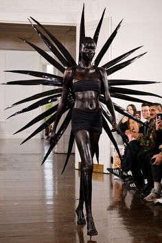 a model walks down the runway in a black outfit with large spikes on her head