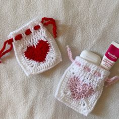 two crocheted items are laying on a white blanket and one has a bottle in the shape of a heart