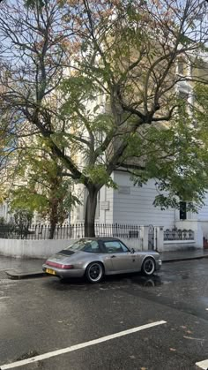 a car parked in front of a tree on the side of a road next to a white building