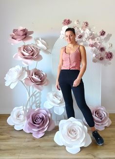 a woman standing in front of paper flowers on a wall and posing for the camera