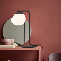 a table lamp sitting on top of a wooden table next to a mirror and books