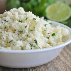 a white bowl filled with food sitting on top of a wooden table next to limes