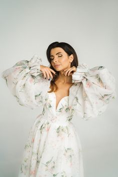 a woman in a white floral dress posing for the camera with her hands on her head