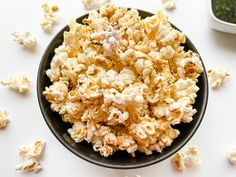 a bowl filled with popcorn sitting on top of a white table next to a cup