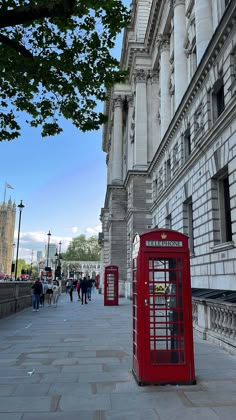 a red phone booth sitting on the side of a road next to a tall building