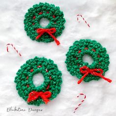 three crocheted christmas wreaths sitting on top of a white blanket with candy canes