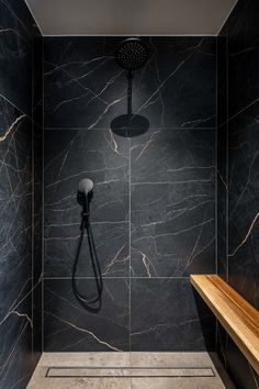 a shower head in a black and white tiled bathroom with wooden bench next to it