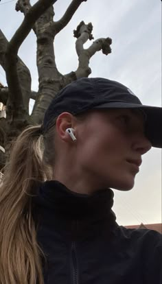 a woman with ear buds is standing in front of a tree