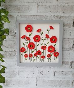 a white frame with red flowers in it on a brick wall next to a green plant