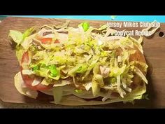 a sandwich with lettuce and tomatoes on it sitting on top of a cutting board