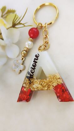 a gold keychain with a red and white letter on it next to flowers