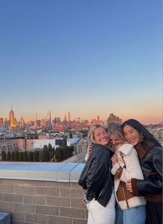 three women standing on top of a building in front of a city skyline at sunset