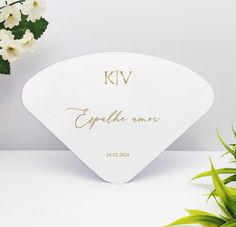 a white plate with gold lettering on it next to some flowers and a potted plant