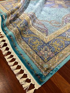 a blue and yellow rug with tassels laying on top of a wooden floor